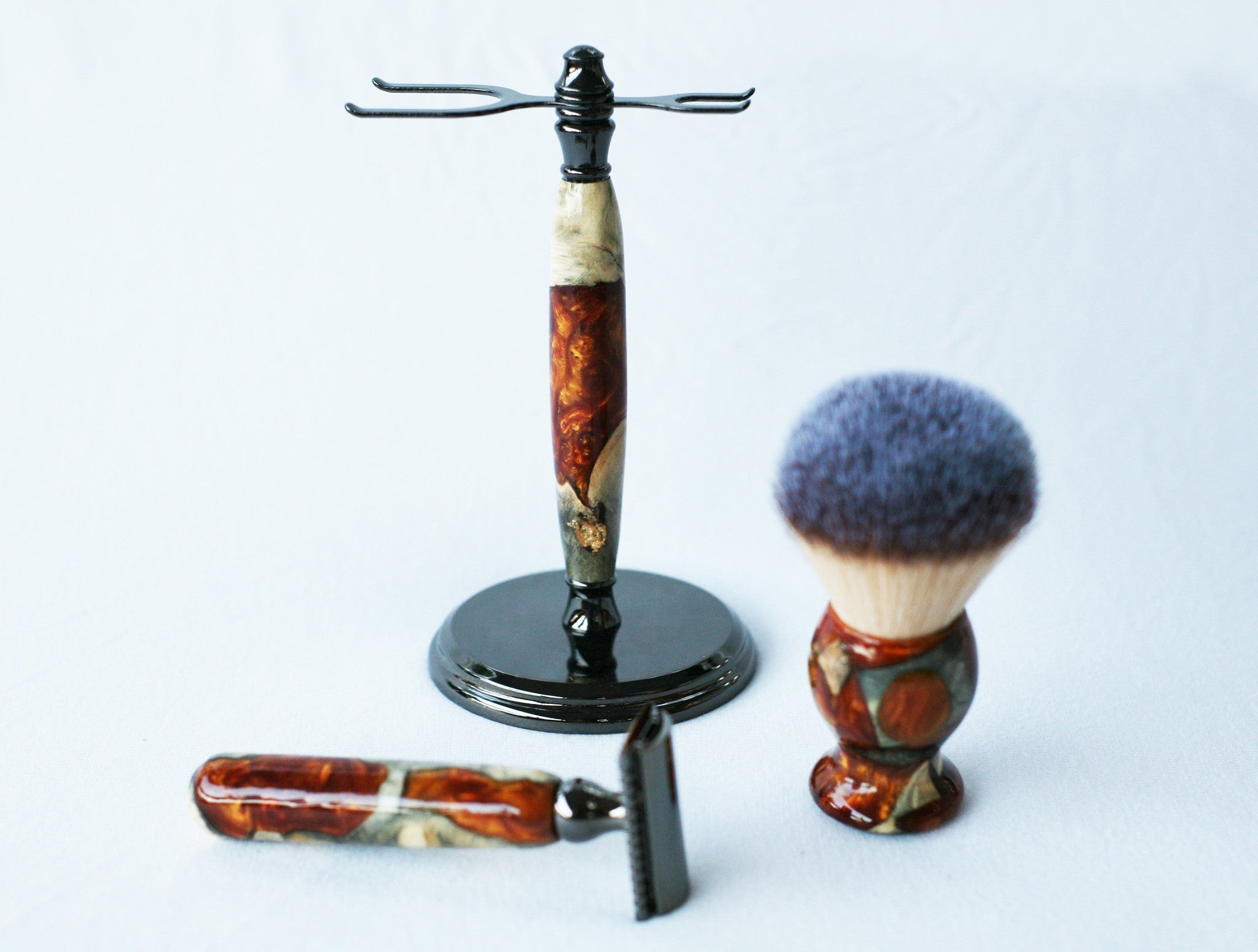 Rasierset aus Buckeye-Maserholz mit Sicherheitsrasierer aus Harz in Gold-Rot-Maserung, 26-mm-Rasierpinsel und passendem Rasierständer.